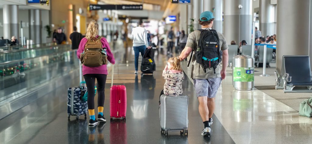 A family of three walks with luggage through an airport hallway.
